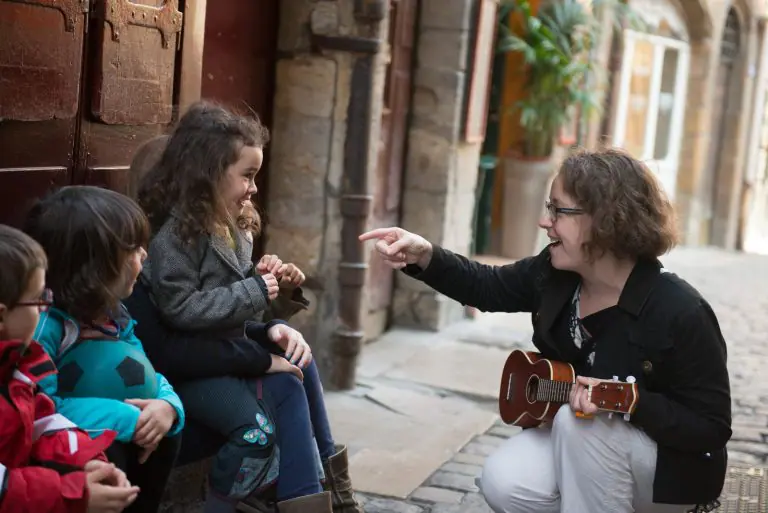 une femme avec un ukukéké montre du doigt une petite fille parmi un groupe d'enfants dans une rue du Vieux Lyon