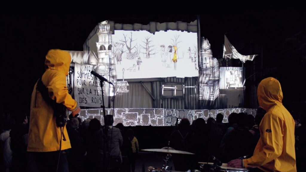 Deux acteurs en ciré autour d'un dispositif de projection dans le spectacle Fantôme 