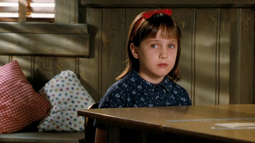 l'actrice mara wilson, enfant, assise à une table dans son rôle de Matilda