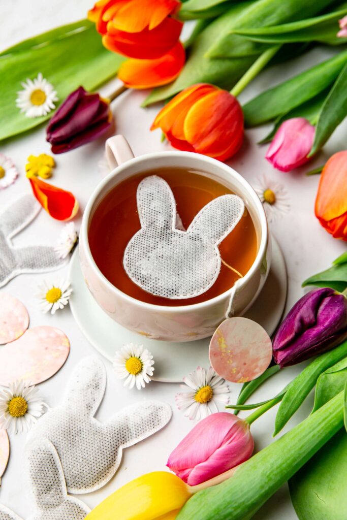 sachet de thé en forme de tête de lapin dans une tasse sur une table décorée de tulipes