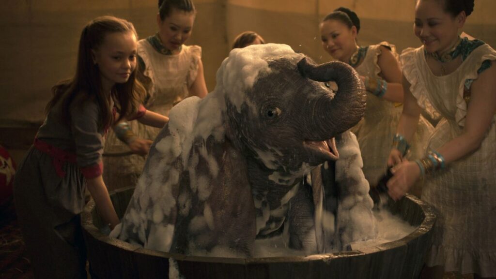 l'éléphant Dumbo en train d'être savonné par un groupe de femmes et une fillette