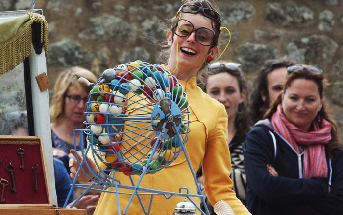 Une femme en jaune et a lunettes devant boulier de loto dans le spectacle La Françoise des jeux